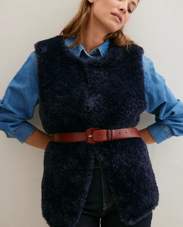 Colete de pêlo negro felpudo com cinto castanho sobre camisa de ganga azul