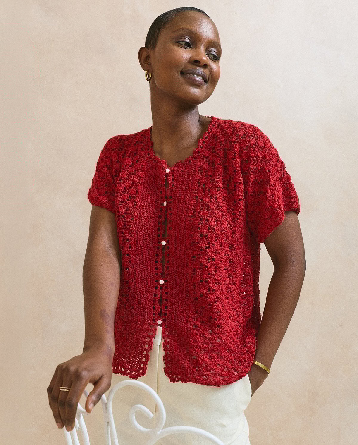 Blusa vermelha de malha com padrão de croché e botões brancos, usada por mulher