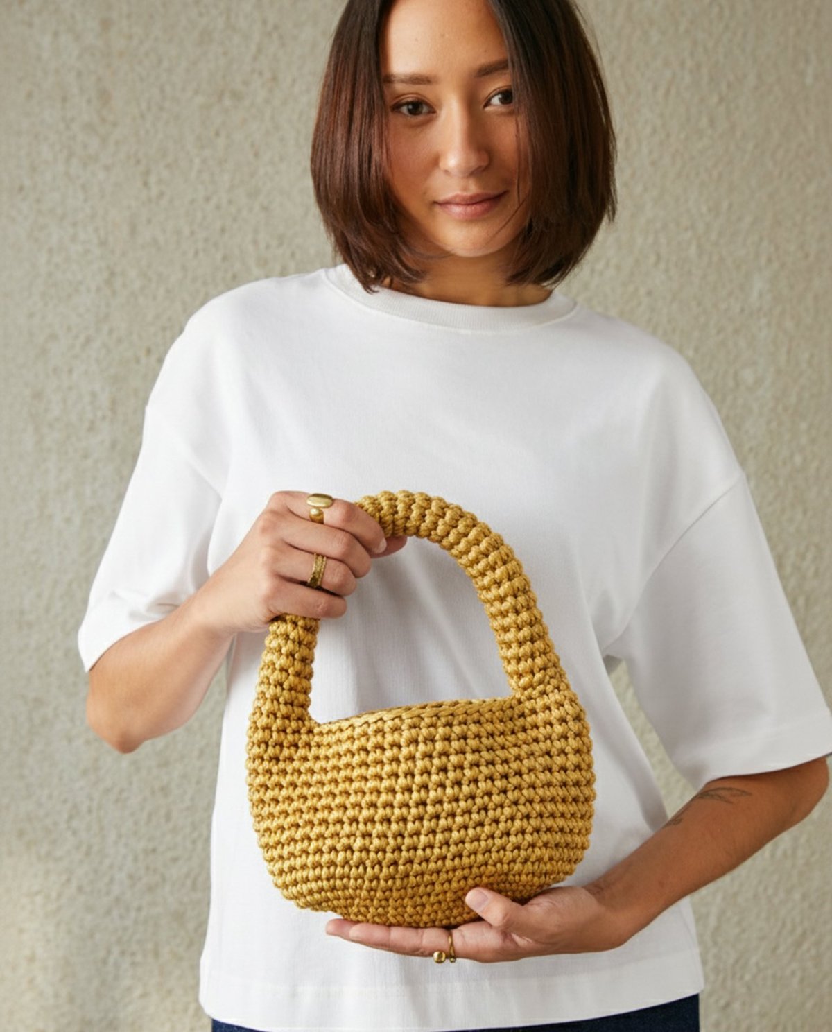 Carteira de mão trançada amarelo mostarda segurada por mulher com t-shirt branca