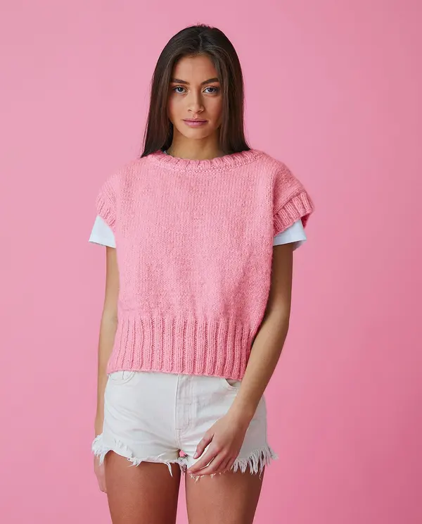 Top rosa de tricô sobre t-shirt branca e calções brancos jeans desfiados com fundo rosa
