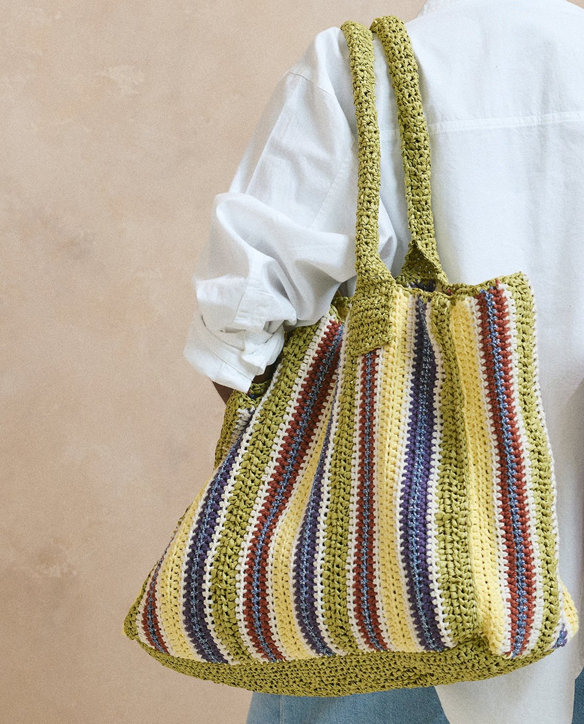 Mala de ombro tricotada com riscas coloridas e alças verdes larga.