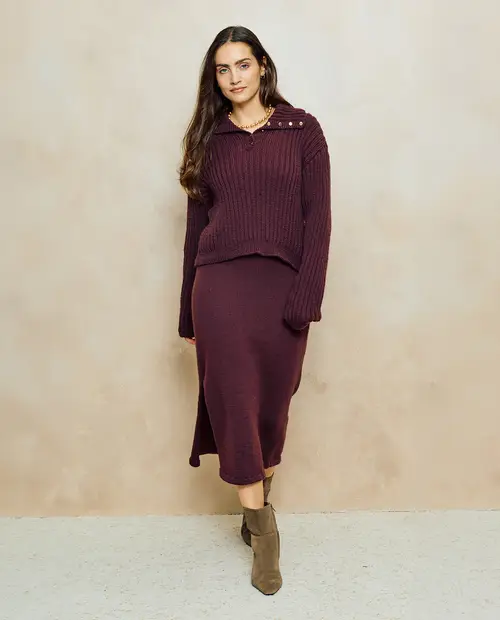 Mulher com conjunto bordeaux de camisola de malha com botões e saia comprida, usando botas castanhas.