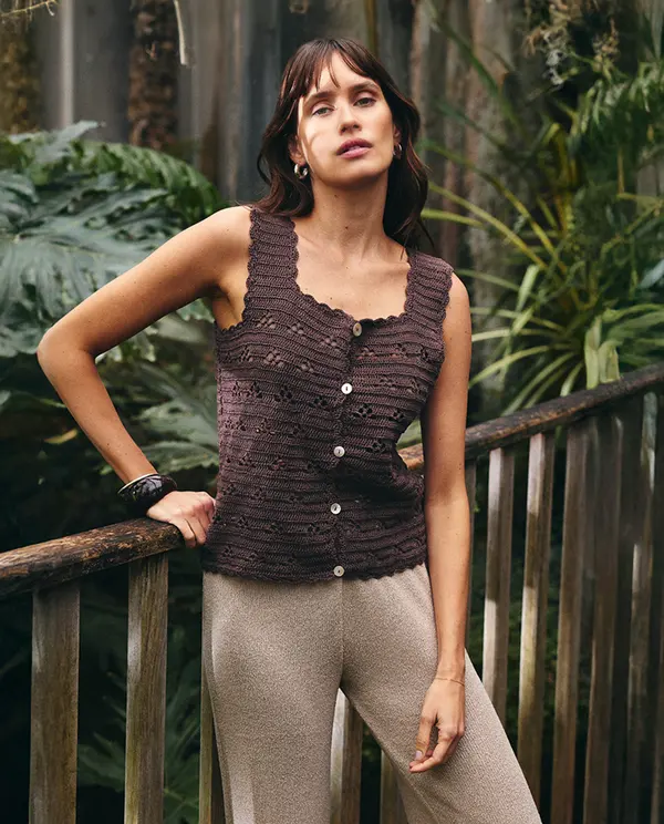 Top de malha castanho escuro com botões e calças bege em ambiente natural