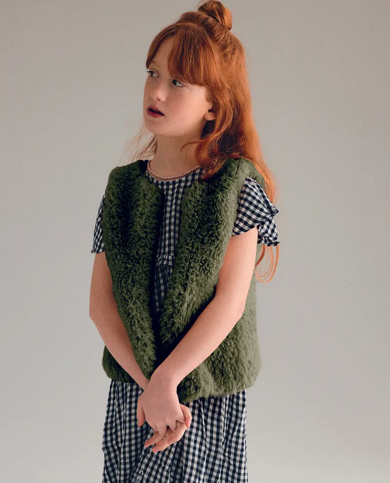 Menina ruiva com vestido xadrez e colete verde peludo