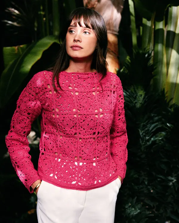 Mulher com suéter coral de crochê com padrão quadrado e calças brancas