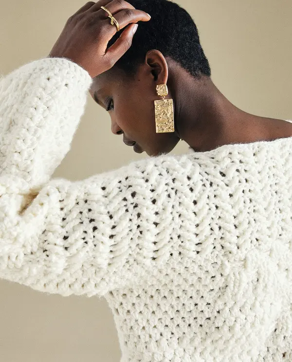 Pessoa de perfil com camisola branca de malha e brincos dourados grandes