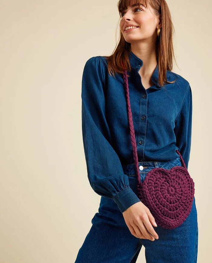 Mulher com camisa azul e bolsa bordô em forma de coração