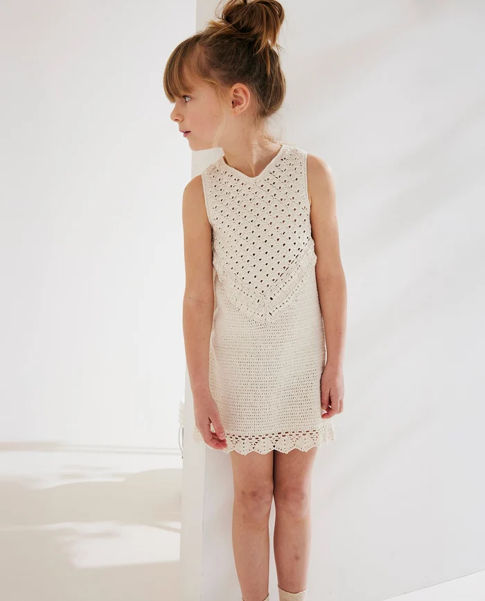Criança com vestido branco de malha, sem mangas, em ambiente interior branco