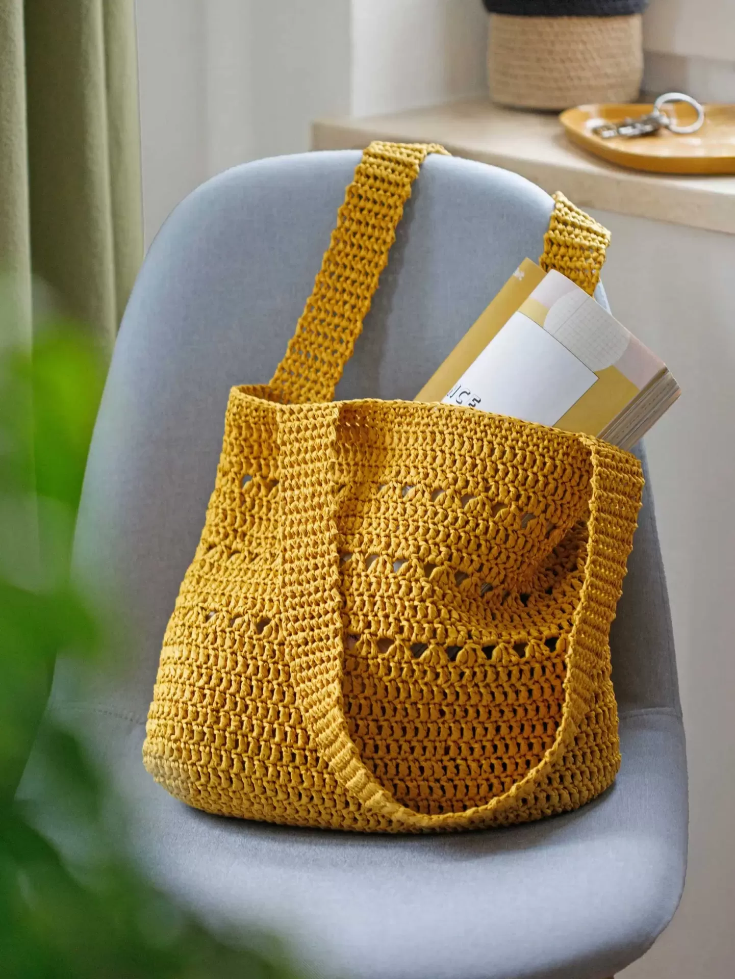 Mala de crochet amarela numa cadeira cinzenta com revista no interior