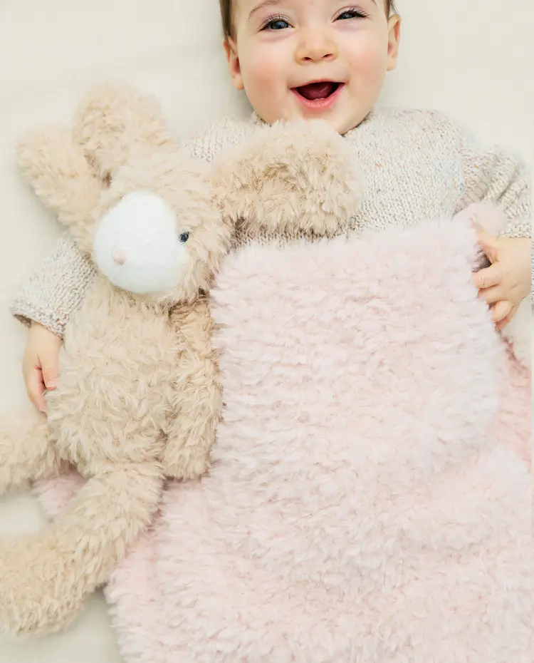 Bebé sorridente com cobertor cor de rosa e peluche de coelho bege