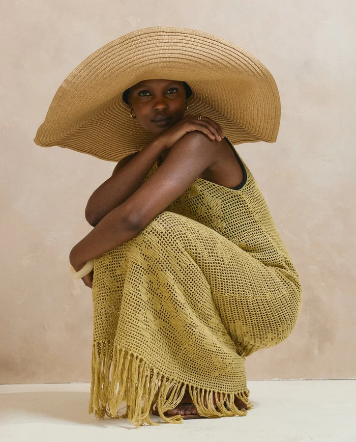 Mulher a usar vestido longo amarelo de malha com franjas e chapéu largo bege