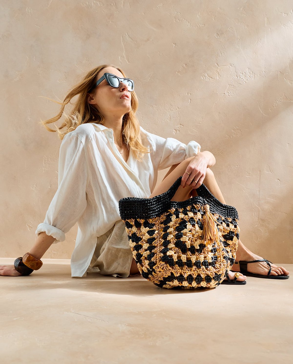 Saco de mão de malha preto e bege com padrão quadriculado junto a mulher sentada com roupa clara