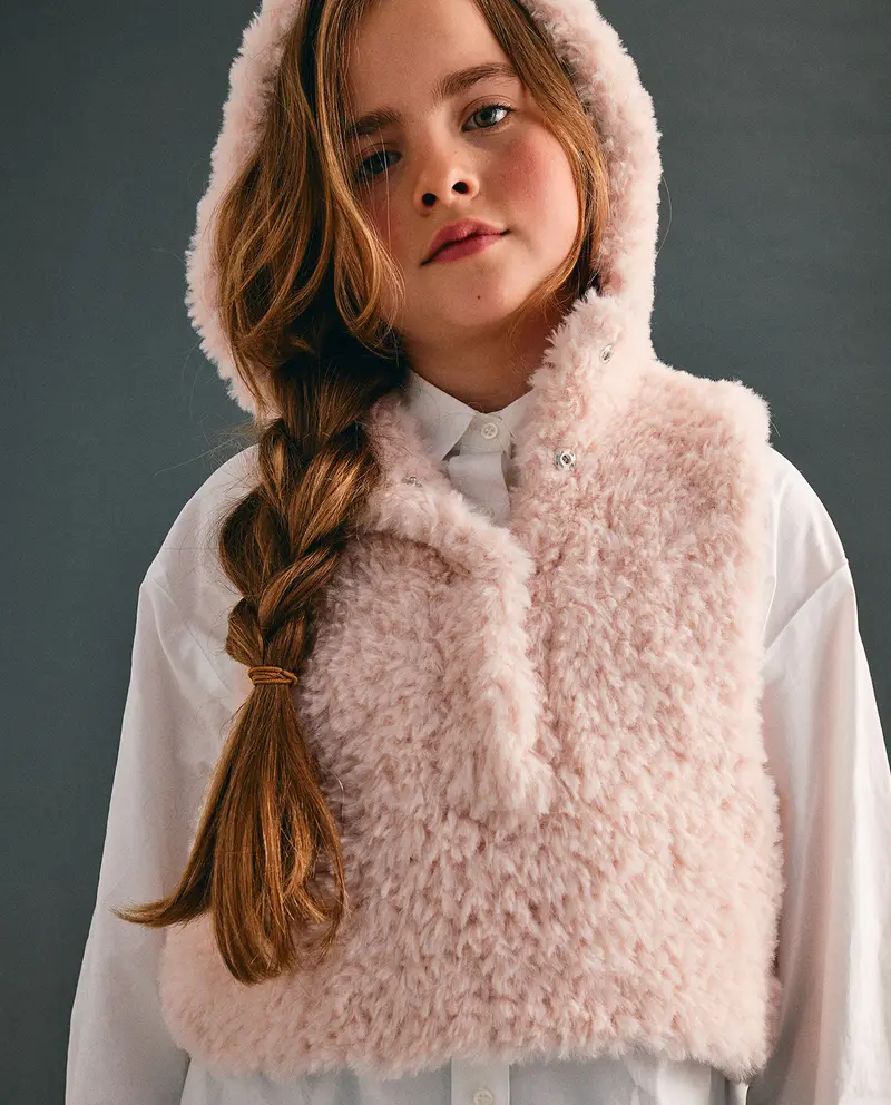 Criança com colete de pelo rosa claro com capuz e camisa branca