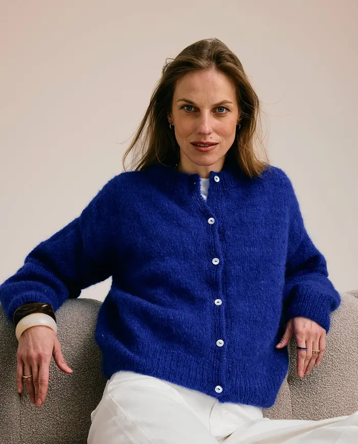 Mulher a usar cardigã azul com botões brancos sentada num sofá beige