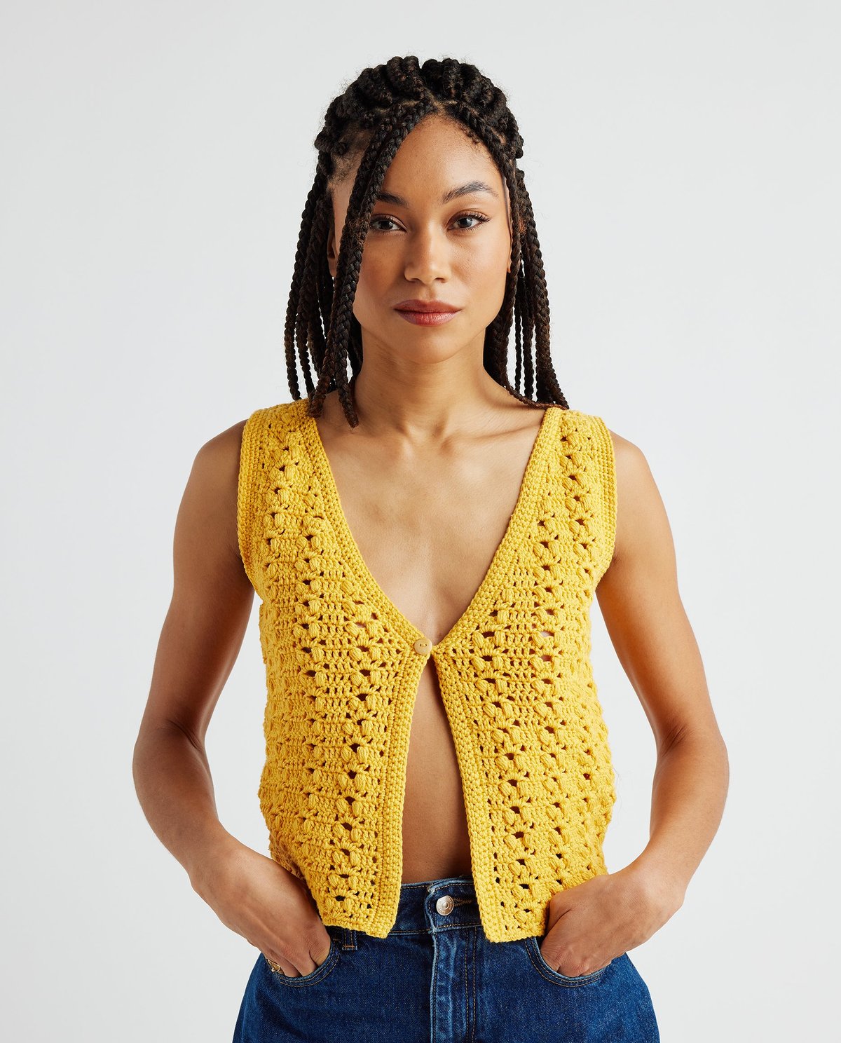 Colete amarelo de malha crochet com botão frontal e jeans azuis