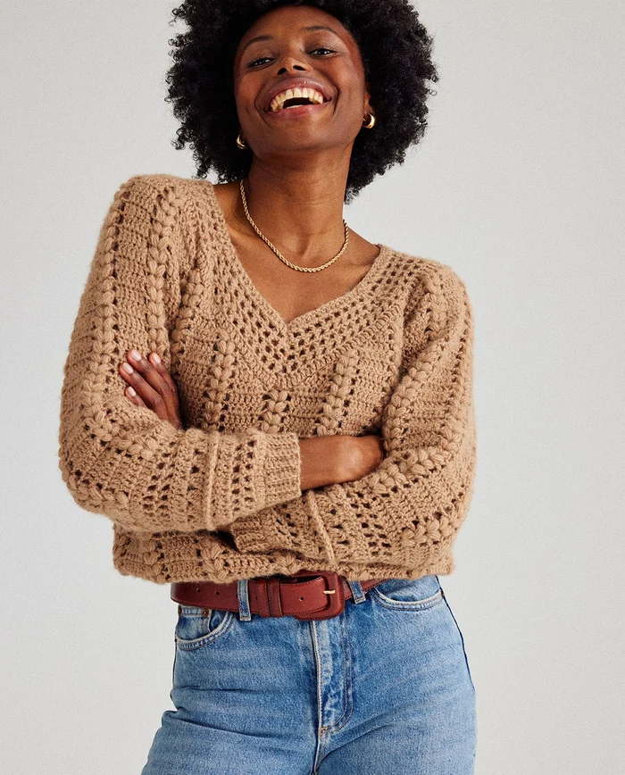 Camisola bege de malha grossa com decote em V, jeans azuis e cinto castanho