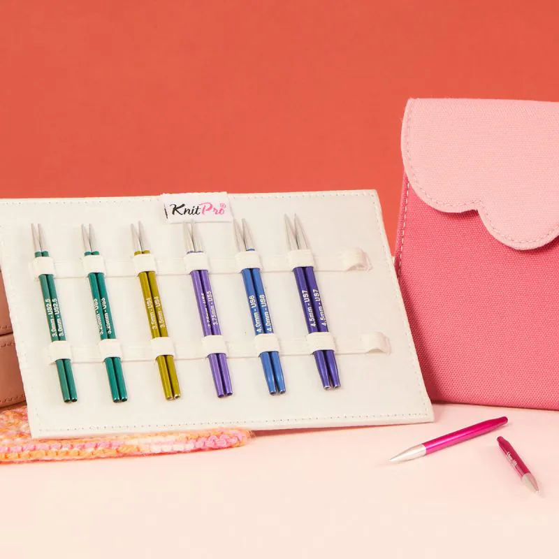 Conjunto de agulhas de tricô metálicas coloridas organizadas em carteira branca com bolsa rosa ao lado.