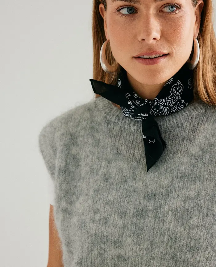 Mulher com lenço preto estampado, camisola cinza felpuda e brincos prateados