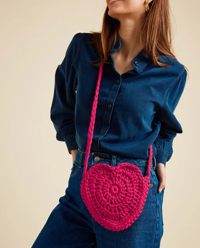 Bolsa de coração rosa forte tricotada com alça, mulher com camisa e jeans azuis