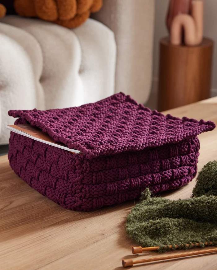 Caixa quadrada em croché roxa sobre mesa de madeira clara