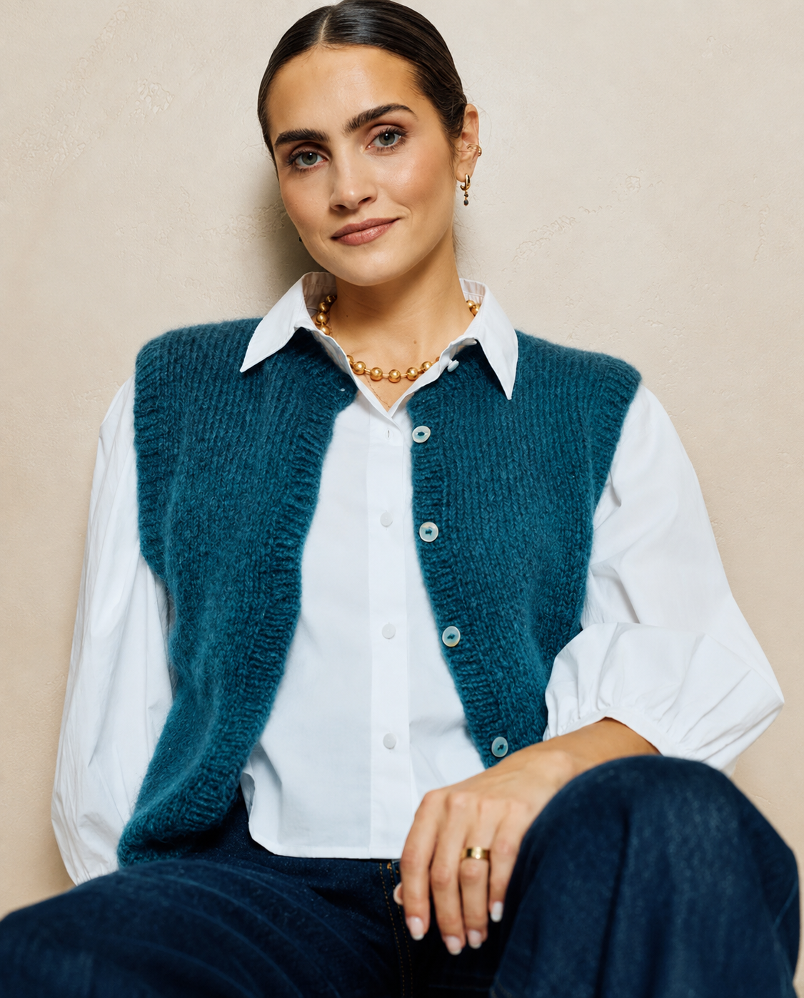 Mulher com colete azul-escuro e camisa branca sentada