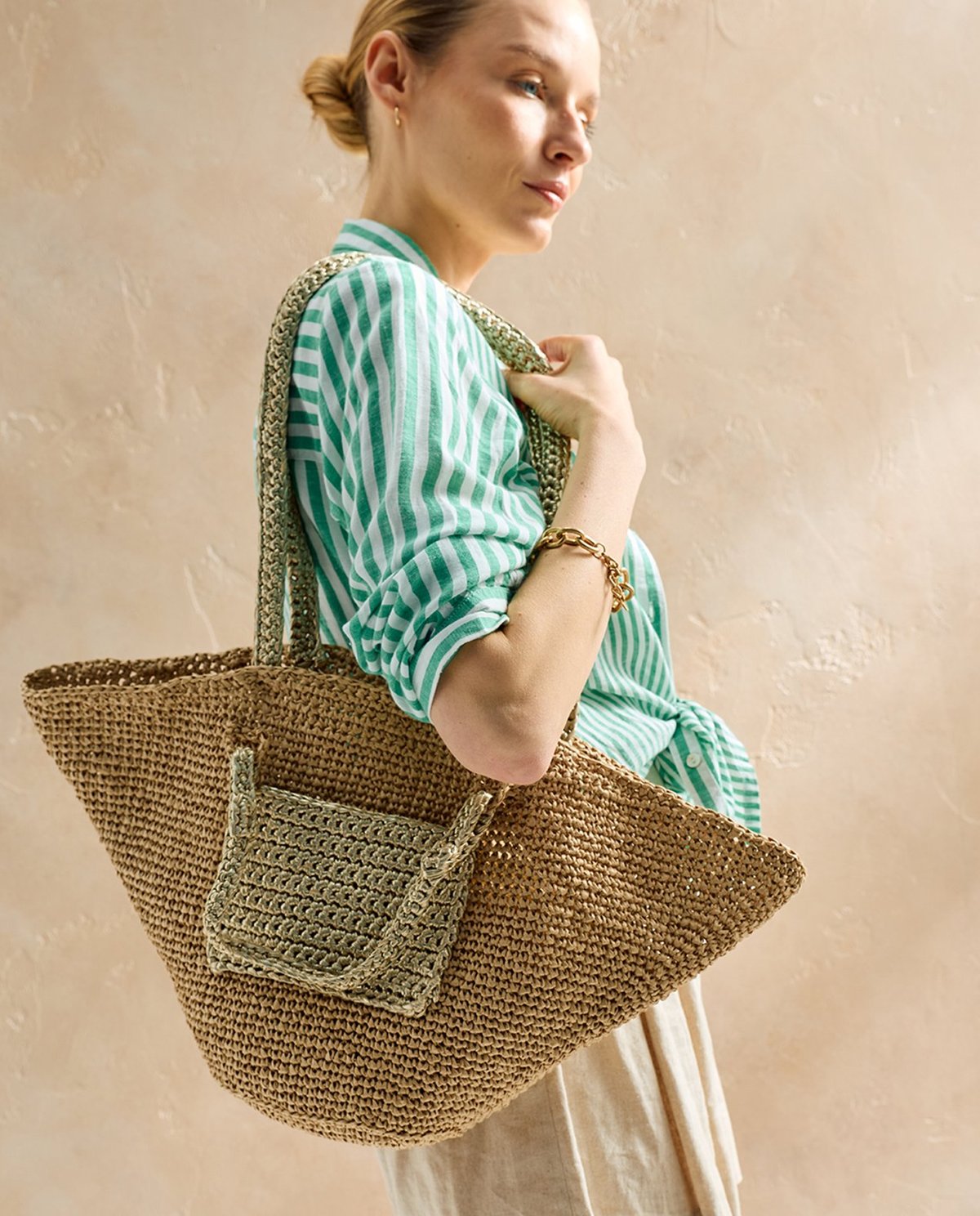 Mala de crochê bege com bolso usado por mulher com camisa riscada verde e branca.