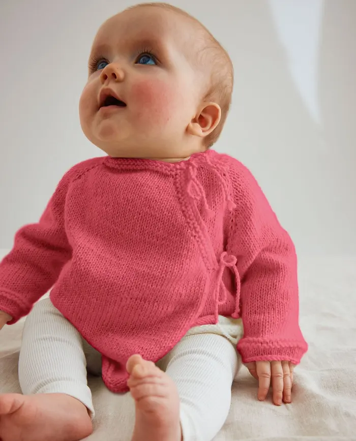 Bebé com camisola rosa de malha e calças brancas sentada