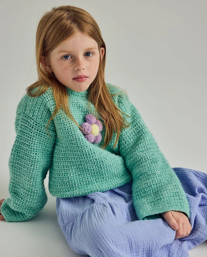 Menina com suéter verde e saia azul clara sentada.