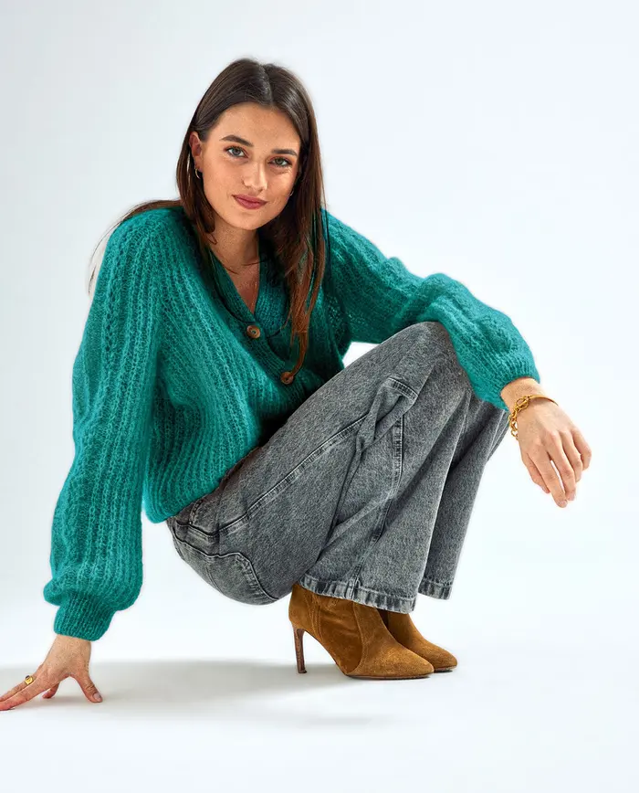 Mulher a usar cardigan verde, jeans cinzentos e sapatos de salto cor mostarda sentada