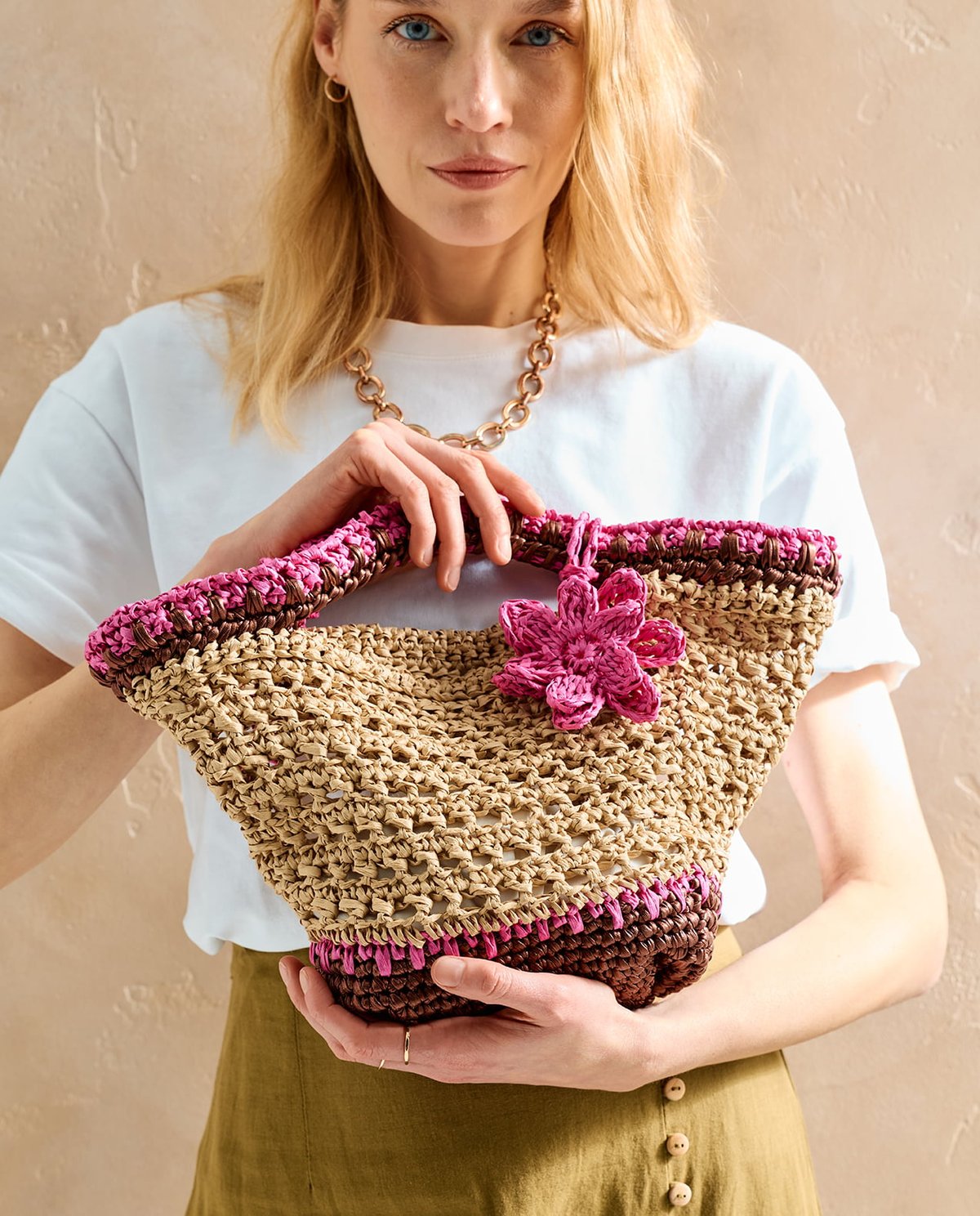 Mala artesanal de ráfia em tons bege, castanho e rosa com flor decorativa rosa.