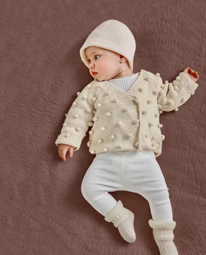 bebé com conjunto creme de malha de pompons e gorro