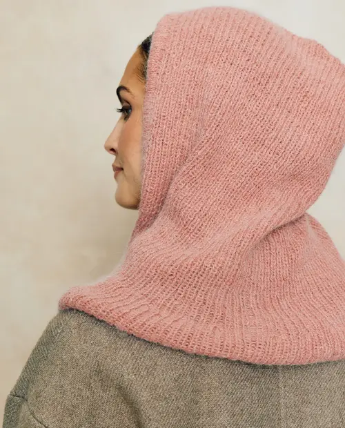 Lenço de malha rosa claro numa mulher com casaco cinza sobre fundo bege