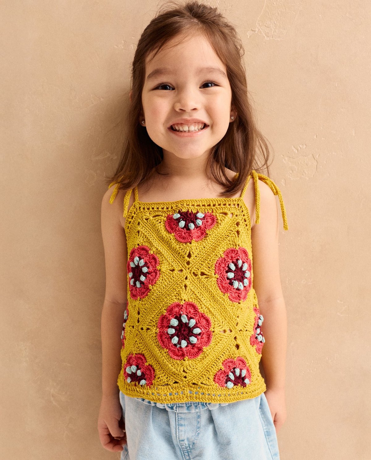 Camisola de crochet amarela com flores vermelhas usadas por criança