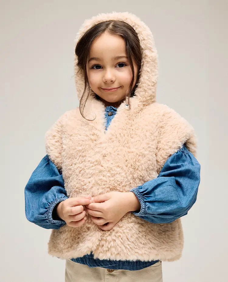 Criança com colete de pelo sintético creme e camisa azul