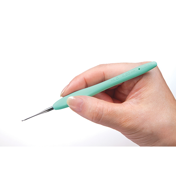 Agulha de croché com cabo verde água segurada por uma mão sobre fundo branco