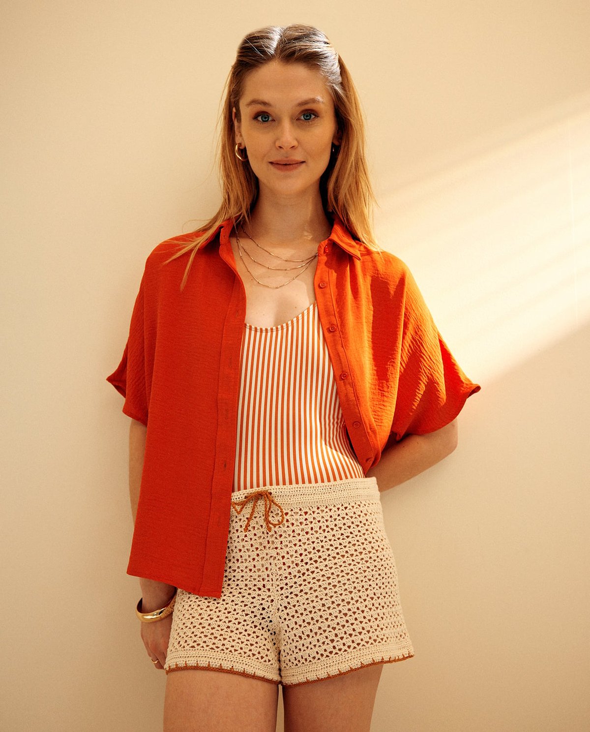 Mulher com roupa casual em tons laranja e creme contra parede branca