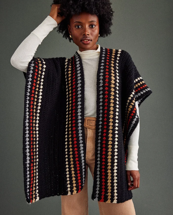 Mulher com poncho de malha preta com riscas coloridas