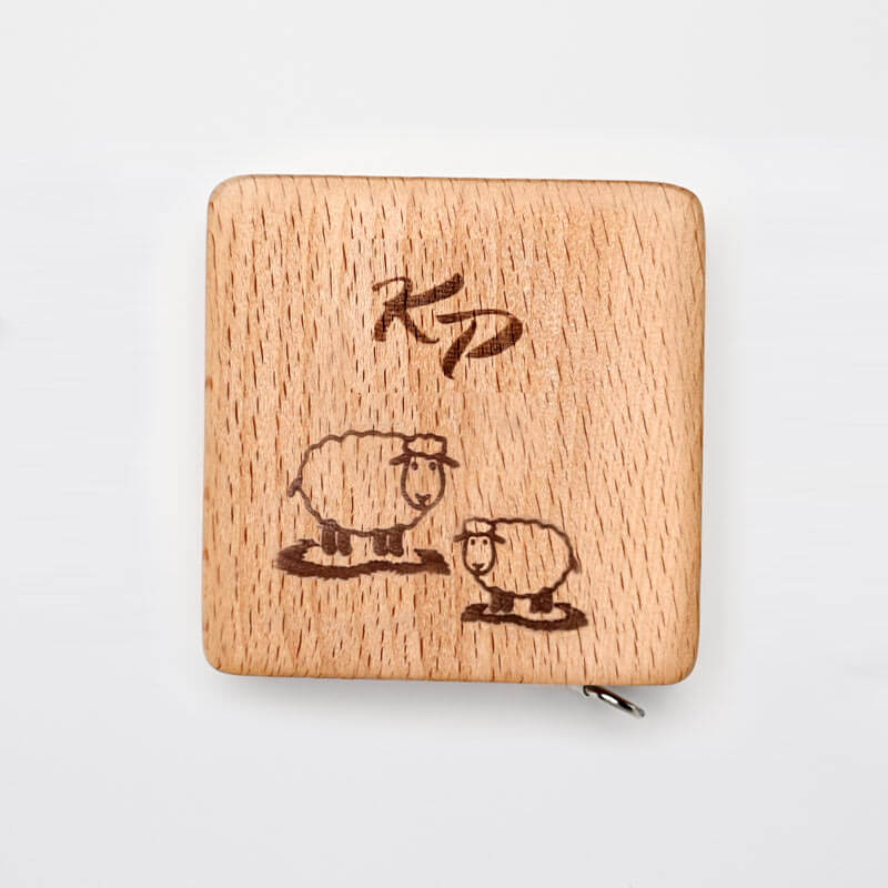 Caixa quadrada de madeira clara com gravura de ovelhas e as letras 'KD'