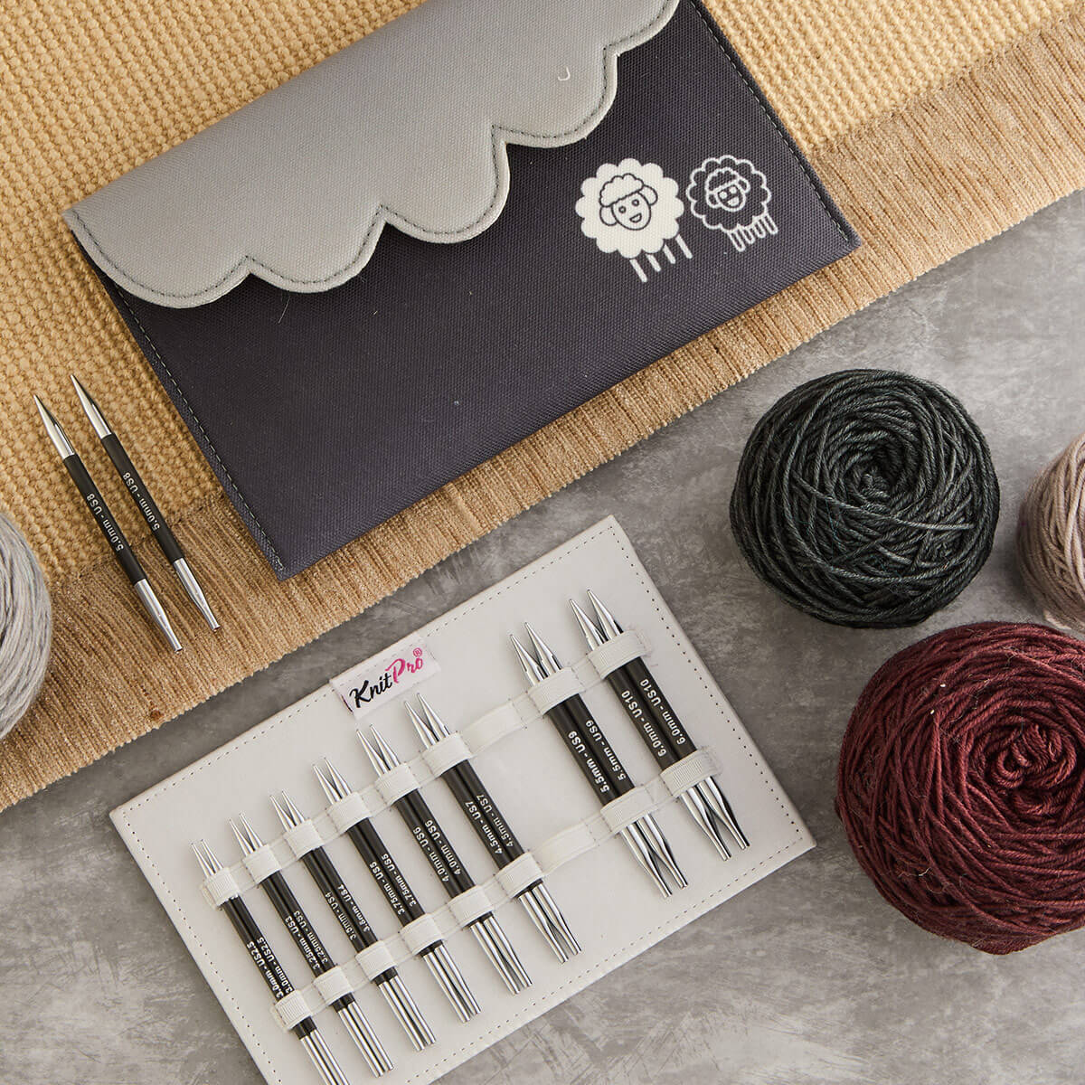 Estojo cinza de agulhas de tricot junto a carretéis de fios coloridos