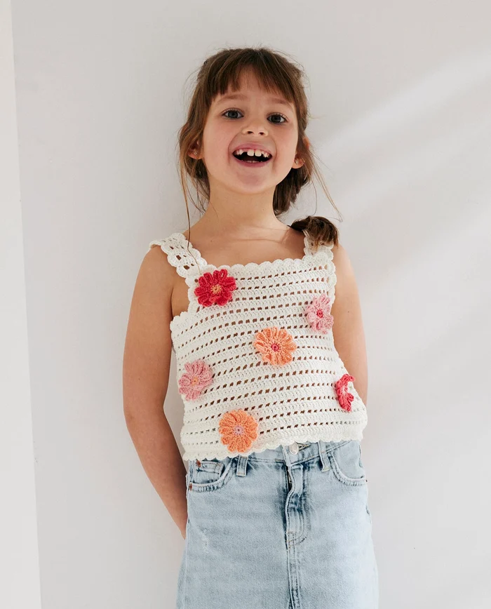 Menina com camisola de alças em crochet branco com flores coloridas e saia de ganga azul clara