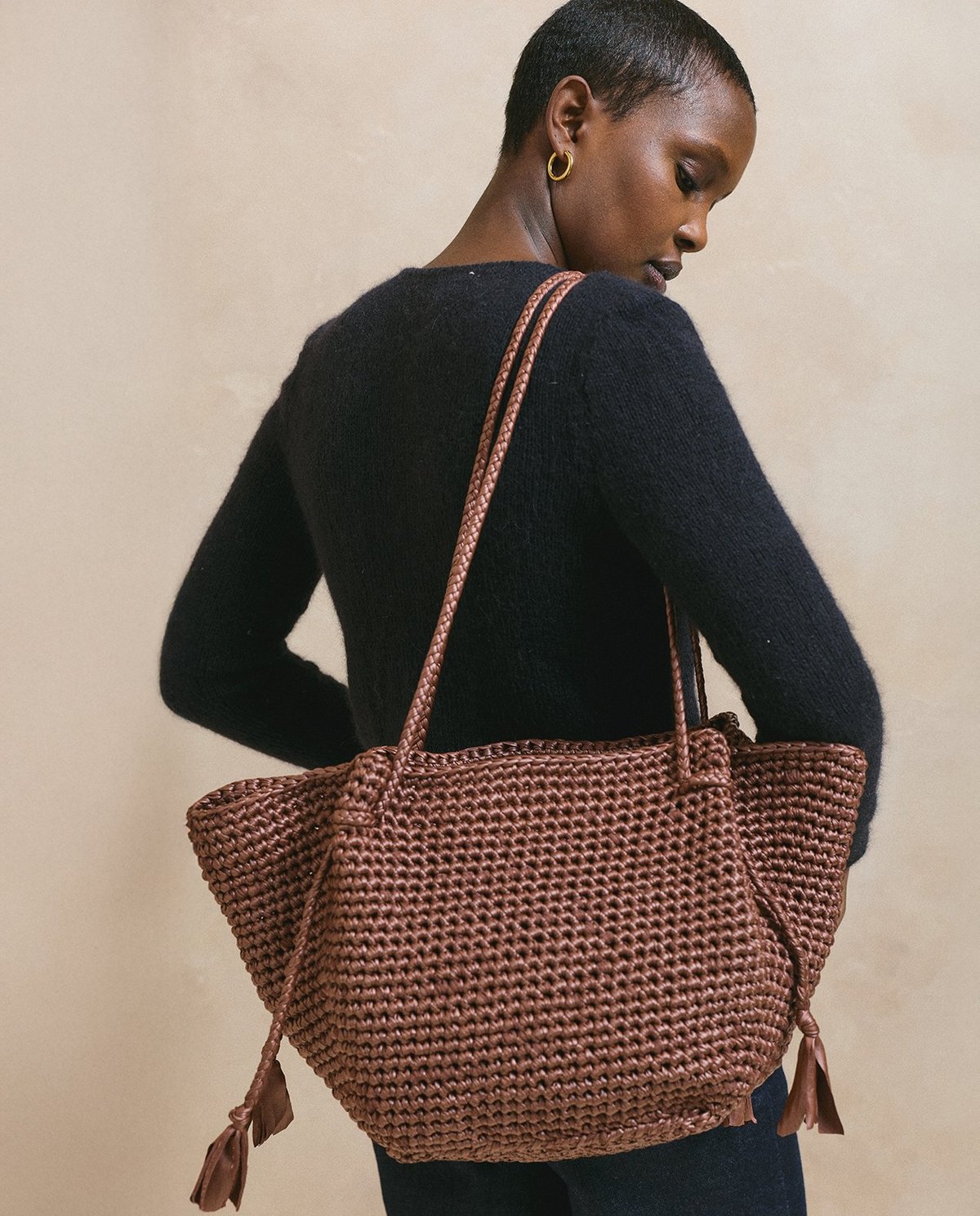 Mala castanha trançada com alças longas sobre o ombro de mulher com camisola preta