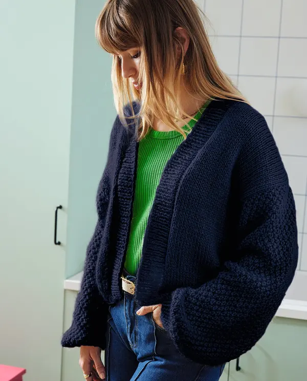 Mulher com casaco de malha azul escuro e camisola verde em cozinha