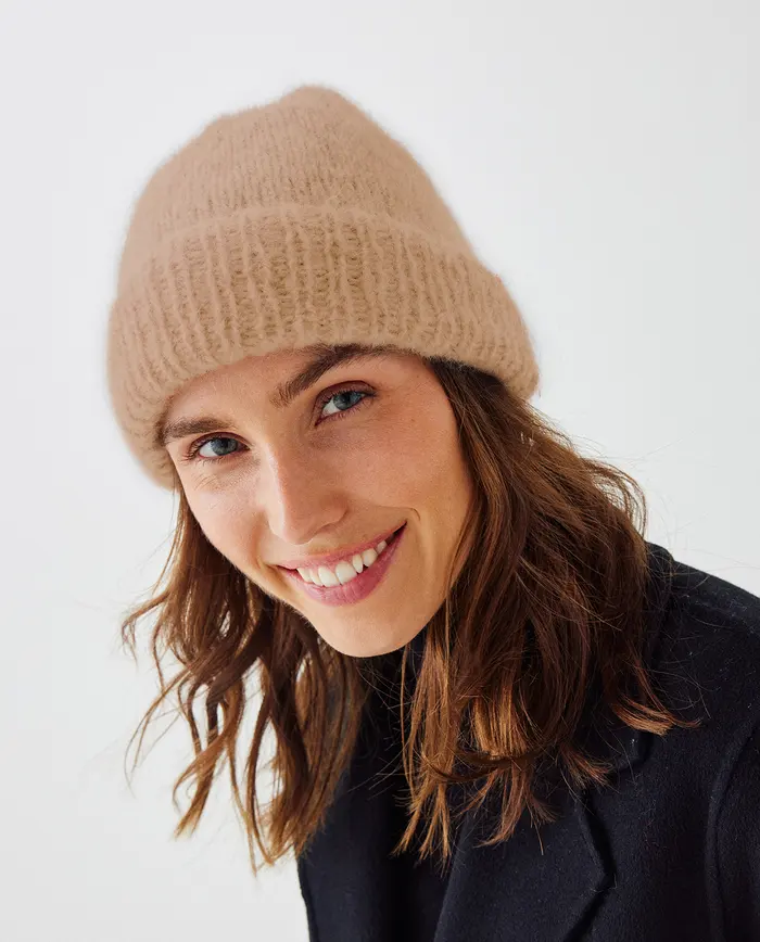 Mulher sorridente com gorro bege e casaco preto