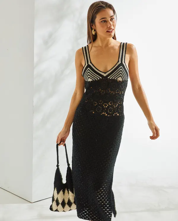 Mulher a usar vestido longo de malha preta com padrão geométrico branco e preto na parte superior e mala preta e branca com padrão xadrez.