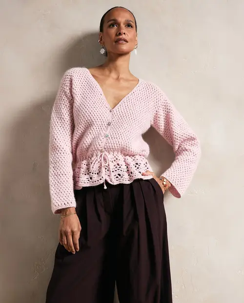 Cardigan rosa claro de malha com botões e cordão, calças pretas largas em fundo neutro