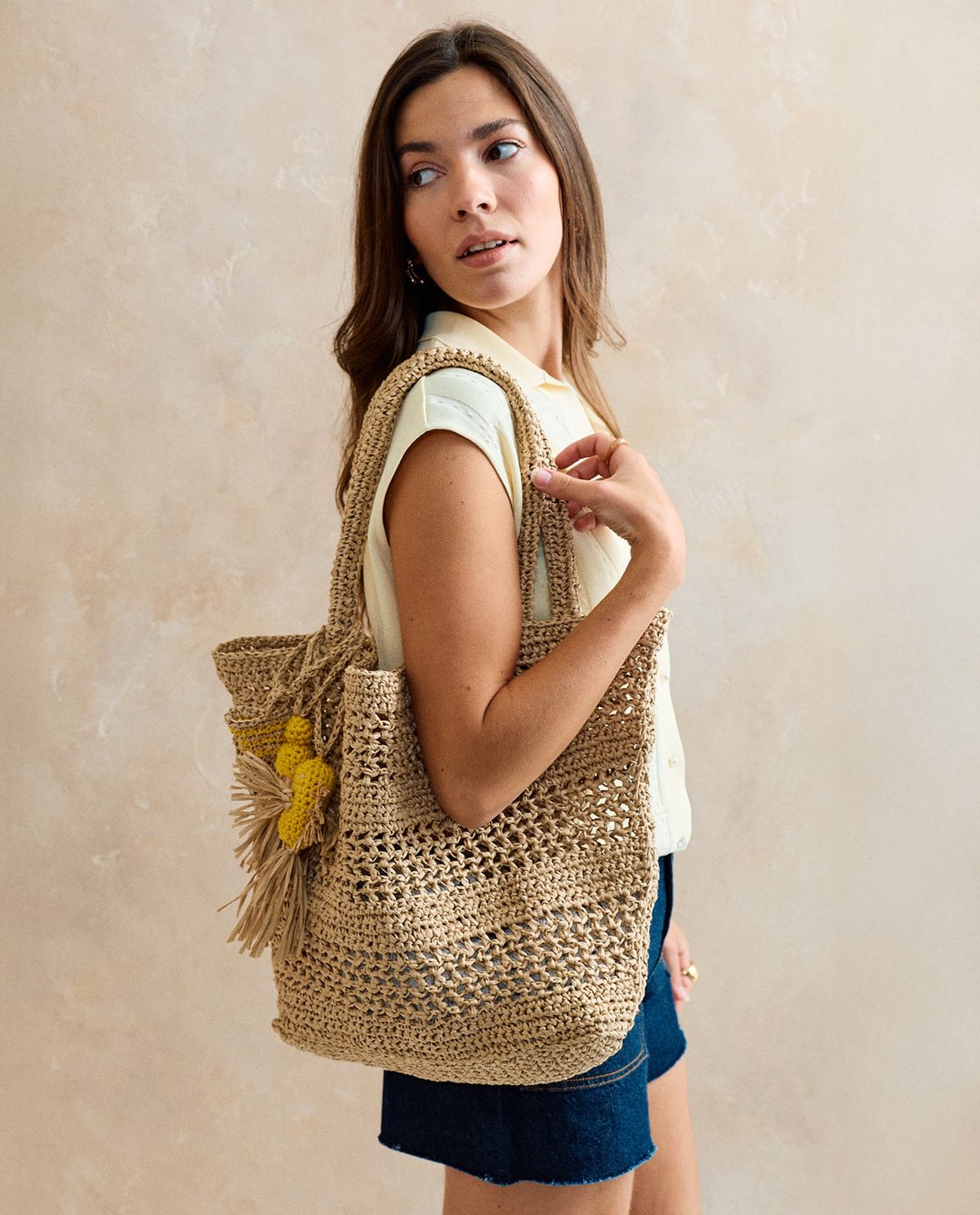 Mulher com mala de tecido trançado bege com adornos amarelos
