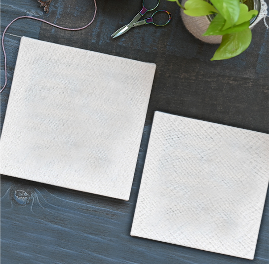 Duas telas brancas sobre mesa escura com planta e tesoura ao lado.