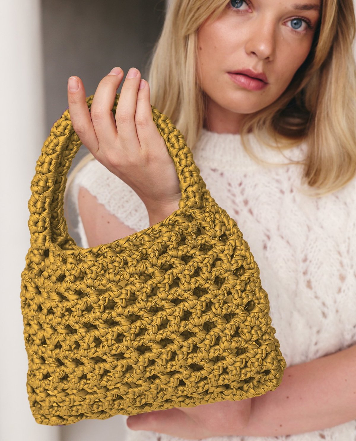Mala de mão tricotada cor mostarda na mão de mulher loira com camisola branca