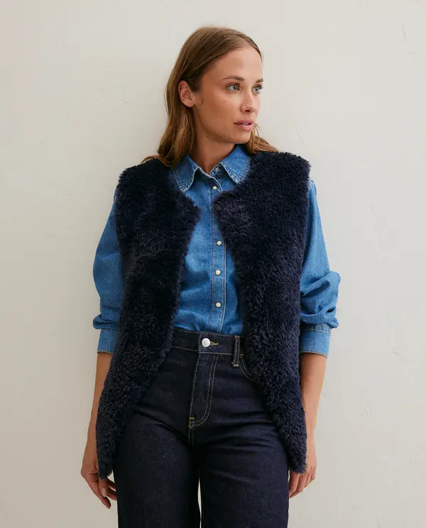 Mulher a usar colete azul escuro de pelo sobre camisa azul e calças escuras