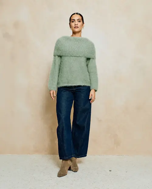 Mulher com camisola de malha verde clara e calças de ganga largas azuis